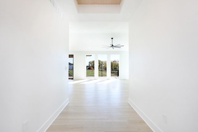 corridor featuring light wood finished floors, baseboards, and a raised ceiling