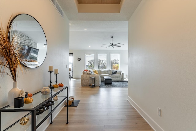 hall featuring a raised ceiling, visible vents, baseboards, and wood finished floors