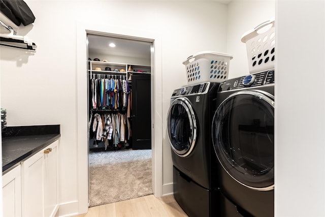 washroom featuring washing machine and dryer, light carpet, cabinet space, and light wood finished floors