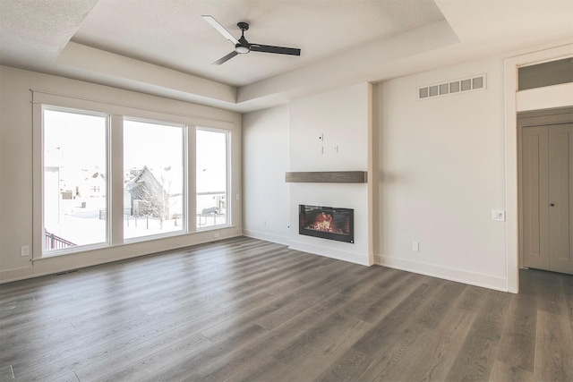 unfurnished living room featuring ceiling fan, a tray ceiling, and dark hardwood / wood-style flooring