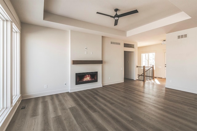 unfurnished living room with a tray ceiling, ceiling fan, and dark wood-type flooring