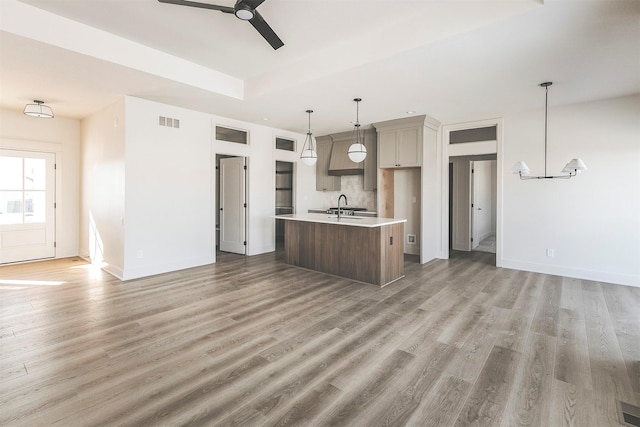 kitchen featuring hardwood / wood-style flooring, a kitchen island with sink, pendant lighting, sink, and ceiling fan with notable chandelier