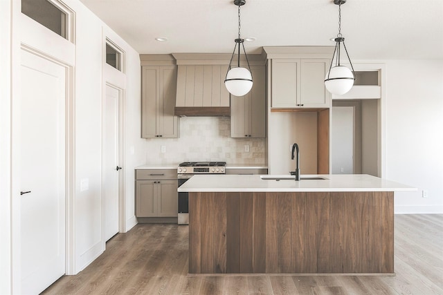 kitchen with a center island with sink, hanging light fixtures, stainless steel range with gas stovetop, backsplash, and sink