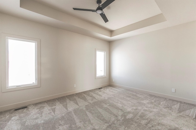 unfurnished room featuring a tray ceiling, light colored carpet, and ceiling fan