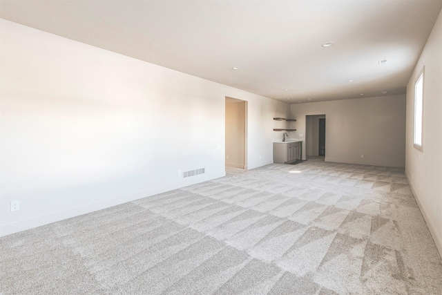 unfurnished living room with sink and light colored carpet