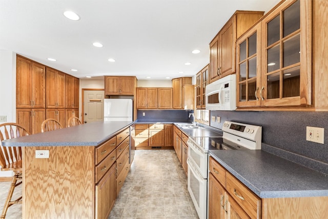 kitchen with sink, a breakfast bar area, backsplash, a center island, and white appliances