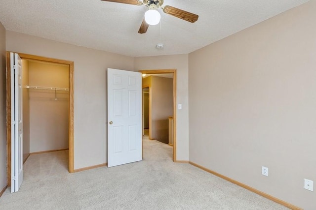 unfurnished bedroom featuring ceiling fan, a textured ceiling, light carpet, a spacious closet, and a closet