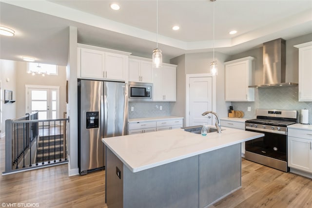 kitchen featuring pendant lighting, wall chimney range hood, sink, appliances with stainless steel finishes, and white cabinetry