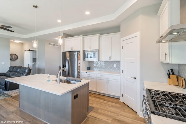 kitchen with wall chimney exhaust hood, white cabinetry, appliances with stainless steel finishes, pendant lighting, and a barn door