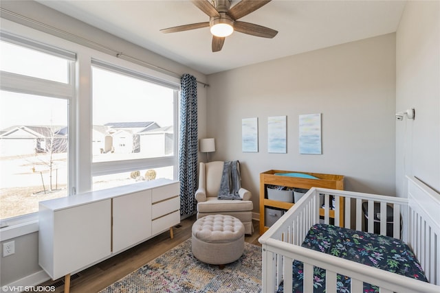 bedroom featuring a crib, dark wood-type flooring, and ceiling fan