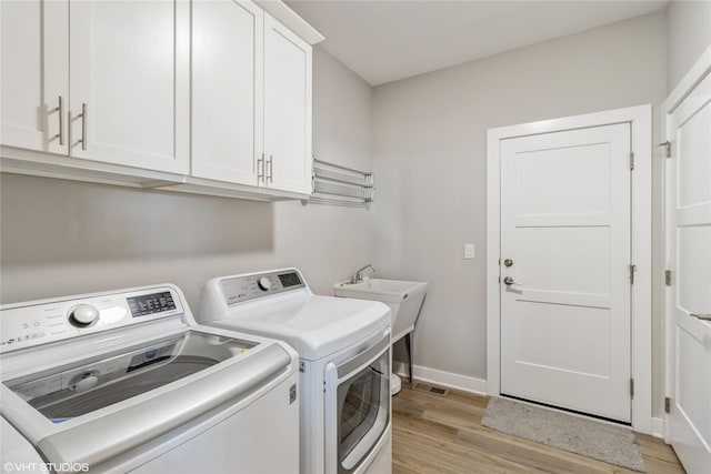 washroom featuring washer and clothes dryer, cabinets, and light wood-type flooring