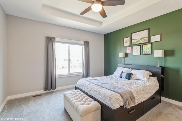 bedroom with light carpet, a tray ceiling, and ceiling fan