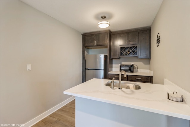 kitchen featuring sink, stainless steel fridge, kitchen peninsula, dark brown cabinets, and light wood-type flooring