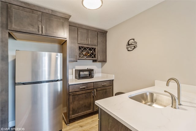 kitchen with dark brown cabinetry, sink, light hardwood / wood-style flooring, stainless steel refrigerator, and light stone countertops