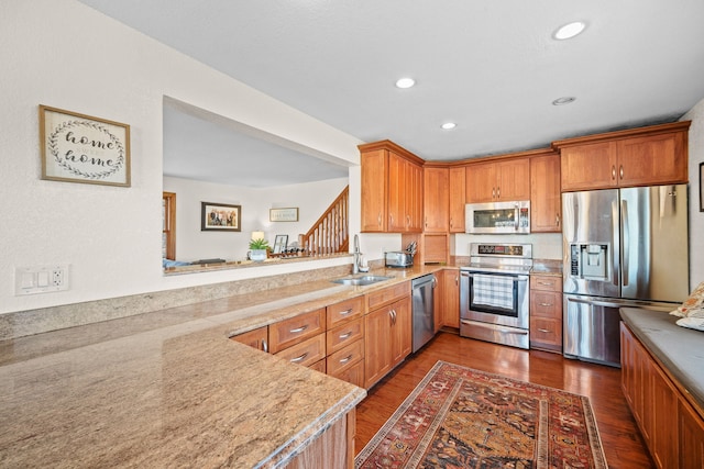 kitchen featuring sink, appliances with stainless steel finishes, dark hardwood / wood-style floors, light stone countertops, and kitchen peninsula