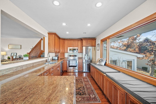 kitchen with appliances with stainless steel finishes, sink, light stone counters, kitchen peninsula, and dark wood-type flooring