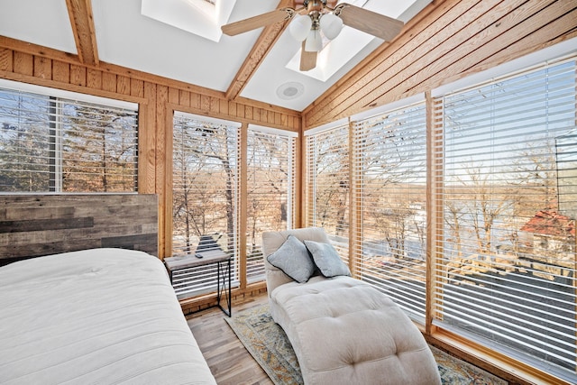 bedroom with hardwood / wood-style flooring, wooden walls, vaulted ceiling with skylight, and ceiling fan