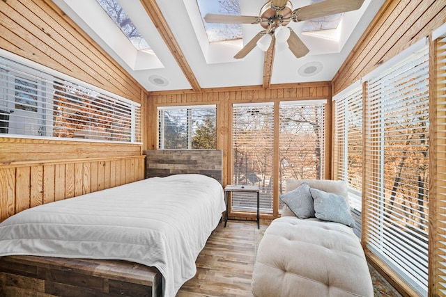 bedroom with hardwood / wood-style floors, lofted ceiling with skylight, ceiling fan, and wood walls