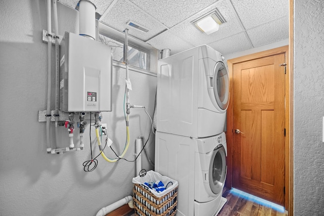 washroom with dark hardwood / wood-style floors, stacked washer and clothes dryer, and tankless water heater