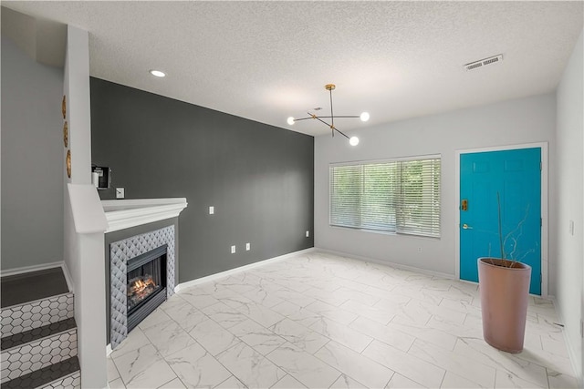 living room with a tiled fireplace, a textured ceiling, and a chandelier