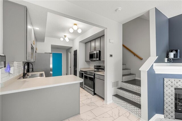 kitchen with tasteful backsplash, sink, gray cabinetry, kitchen peninsula, and stainless steel appliances