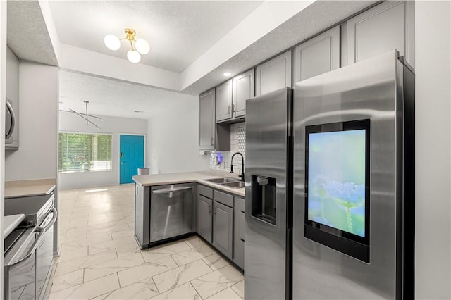 kitchen with kitchen peninsula, sink, gray cabinetry, a tray ceiling, and stainless steel appliances