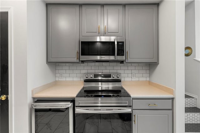 kitchen with backsplash, gray cabinets, and stainless steel appliances