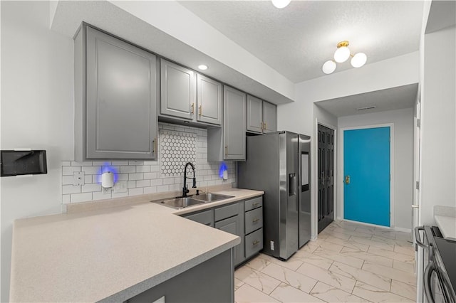 kitchen featuring sink, backsplash, stainless steel fridge, gray cabinets, and stove