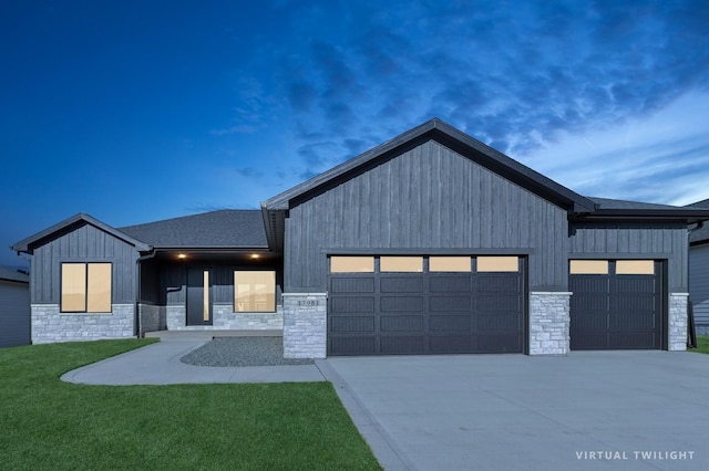 modern farmhouse with a garage, concrete driveway, a front lawn, and stone siding