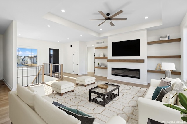 living area with recessed lighting, visible vents, light wood-type flooring, a raised ceiling, and a glass covered fireplace