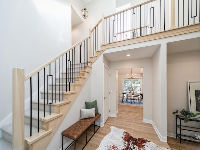 stairway with wood-type flooring, a towering ceiling, and a notable chandelier