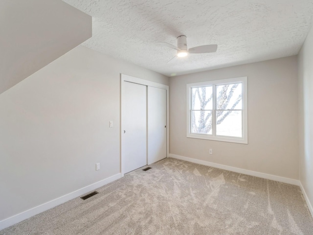 unfurnished bedroom featuring ceiling fan, light colored carpet, a closet, and a textured ceiling