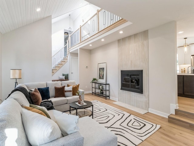 living room featuring high vaulted ceiling, a tile fireplace, and light hardwood / wood-style flooring