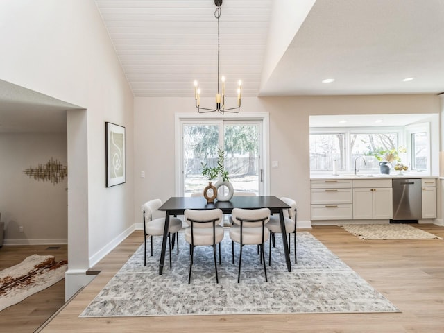 dining room with a notable chandelier, sink, vaulted ceiling, and light wood-type flooring