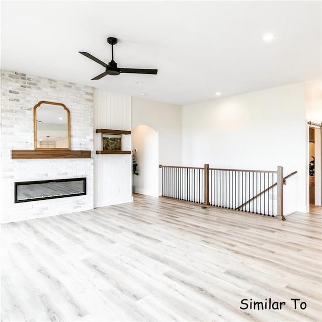 unfurnished living room featuring ceiling fan, a large fireplace, and light wood-type flooring