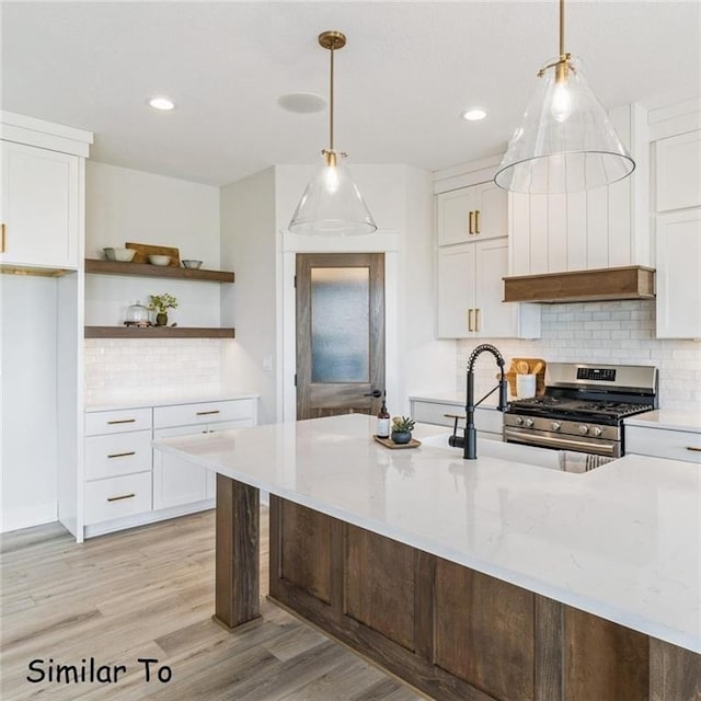 kitchen with pendant lighting, white cabinetry, light stone countertops, stainless steel range with gas stovetop, and light wood-type flooring