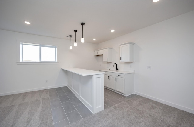 kitchen with a peninsula, baseboards, light countertops, and a sink