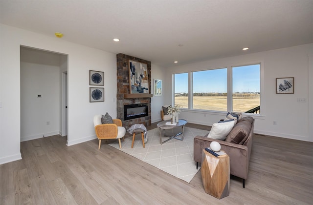 living area with light wood finished floors, recessed lighting, baseboards, and a stone fireplace