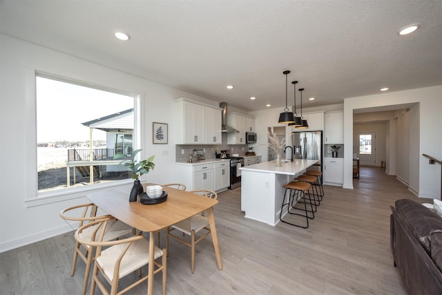 kitchen featuring a sink, white cabinetry, a kitchen breakfast bar, appliances with stainless steel finishes, and wall chimney exhaust hood