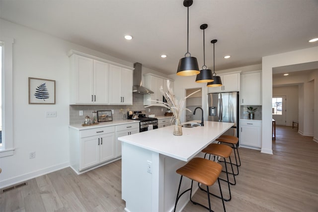 kitchen with sink, white cabinets, hanging light fixtures, stainless steel appliances, and wall chimney range hood