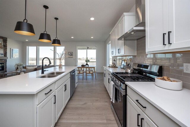 kitchen featuring backsplash, wall chimney range hood, hanging light fixtures, stainless steel appliances, and a center island with sink