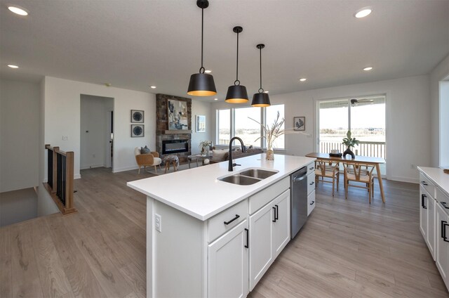 kitchen featuring sink, hanging light fixtures, a fireplace, a center island with sink, and stainless steel dishwasher