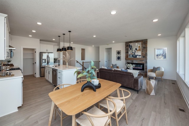 dining room with a textured ceiling, recessed lighting, a large fireplace, baseboards, and light wood finished floors