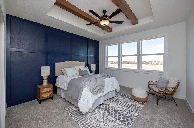 bedroom with light carpet, a tray ceiling, beamed ceiling, and ceiling fan