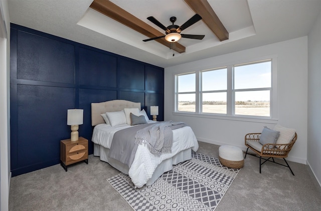 bedroom with light carpet, baseboards, a raised ceiling, and a decorative wall