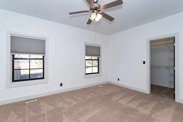 unfurnished bedroom featuring a walk in closet, carpet flooring, ceiling fan, and a closet