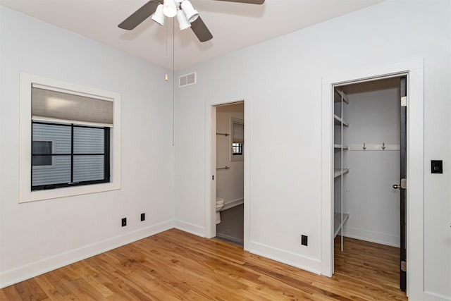 unfurnished bedroom featuring ceiling fan, hardwood / wood-style floors, ensuite bathroom, a walk in closet, and a closet