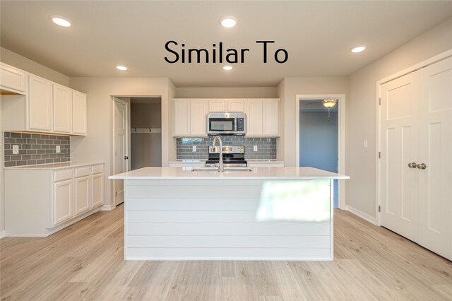 kitchen with stainless steel appliances, white cabinetry, an island with sink, and light hardwood / wood-style flooring