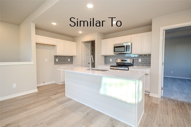 kitchen with stainless steel appliances, an island with sink, sink, and white cabinets