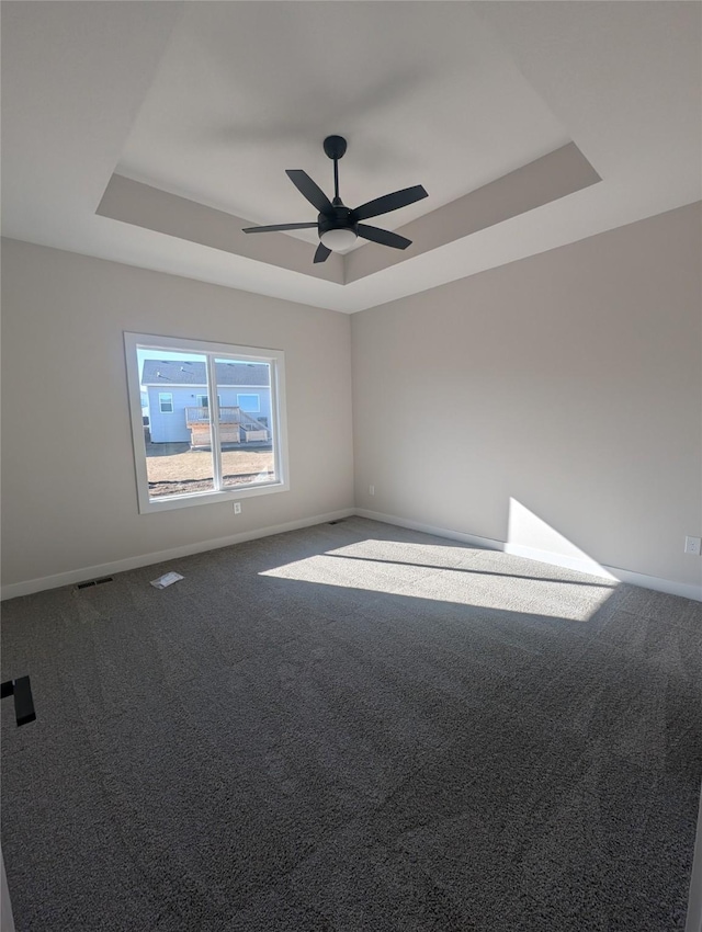 carpeted spare room with a raised ceiling and ceiling fan